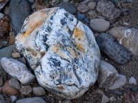 Weißlicher Stein mit grauschwarzen und rostfarbenen Einschlüssen